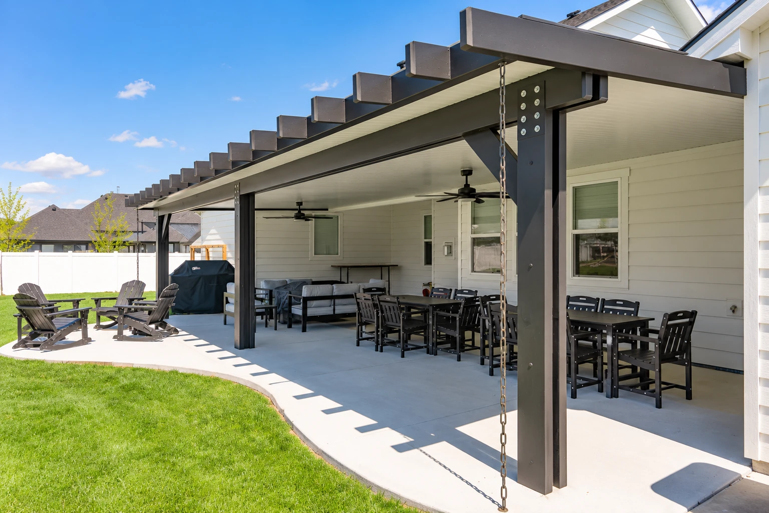 Covered patio with a dark timber roof, ceiling fans and outdoor dining furniture beside a house.