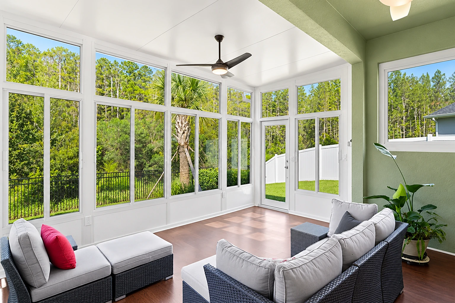 Bright sunroom addition with white-framed windows, wicker seating, and views of a green yard.